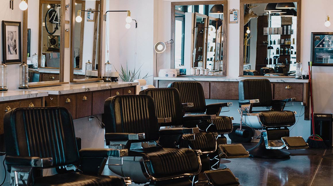 row of black barber shop chairs surrounded by mirrors