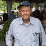man in blue striped shirt and blue hat standing in front of vegetables