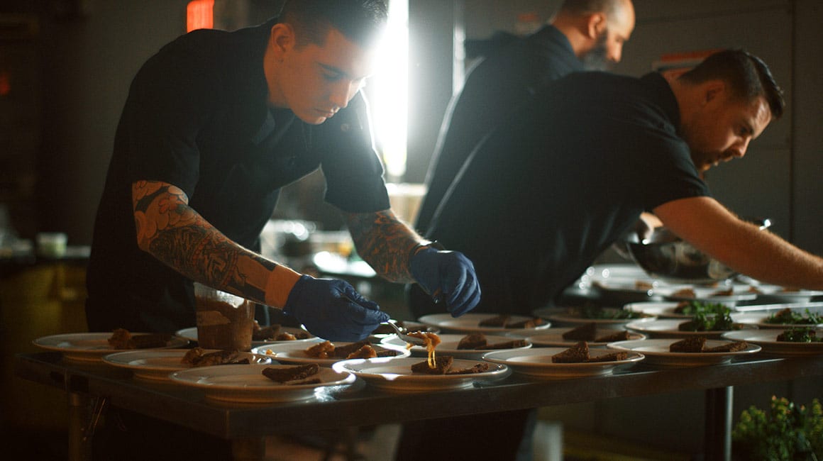 men in black chef uniforms putting food onto plates
